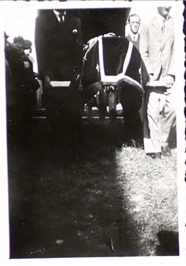 Small black-and-white print: men in suits carry a draped coffin out of the church door into sunlight